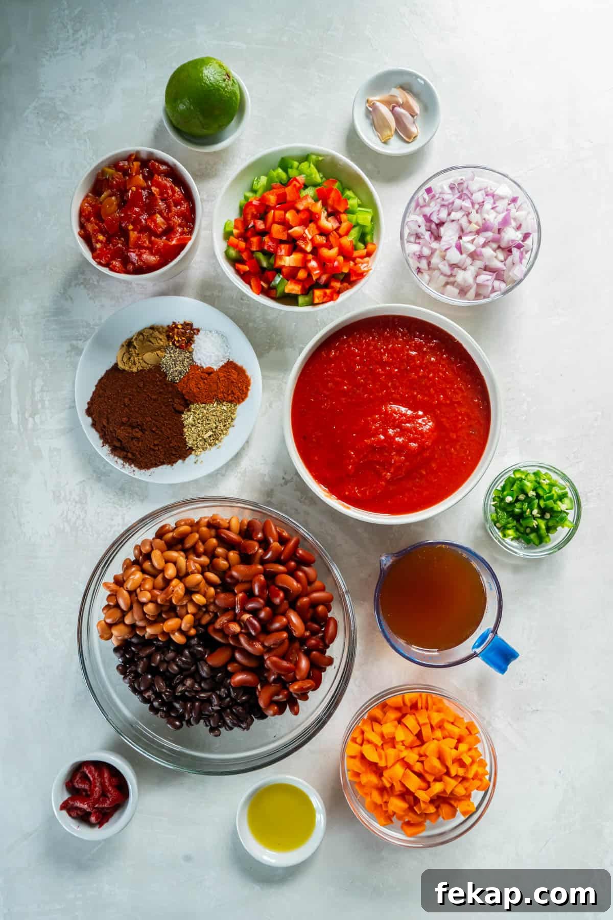 All ingredients for three bean chili arranged in bowls on a white counter.