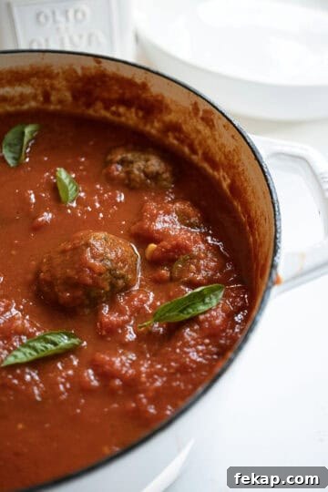 Crispy Italian Pan-Fried Meatballs Recipe 11 A pot filled with sauce and meatballs, garnished with basil.