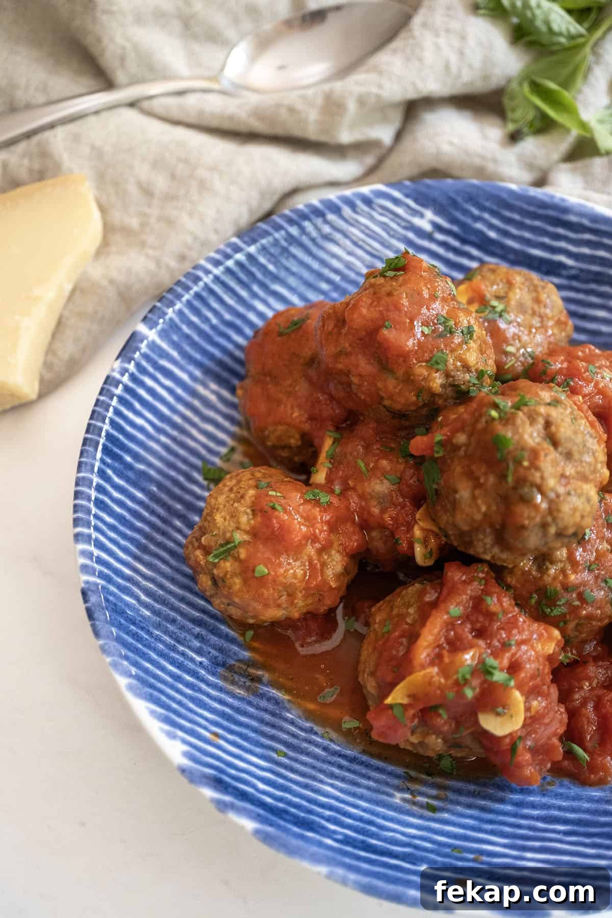 Crispy Italian Pan-Fried Meatballs Recipe 12 Meatballs covered in tomato sauce in a bowl with a block of parmesan cheese on the side.