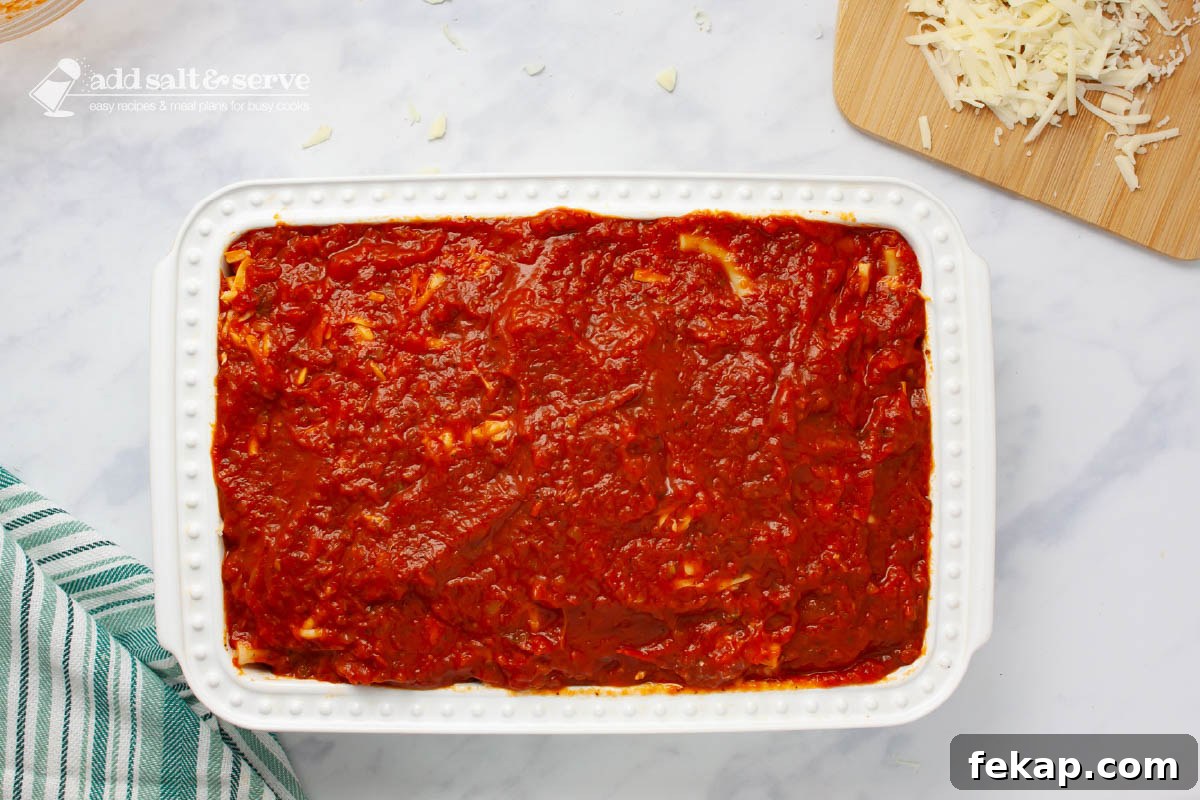 Pan showing a layer of marinara sauce spread over other layers of baked ziti.