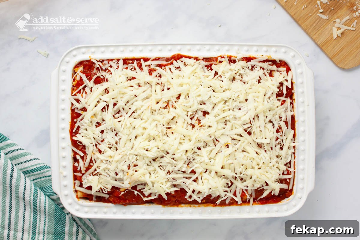 Baking pan showing mozzarella cheese layered over marinara sauce for baked ziti.