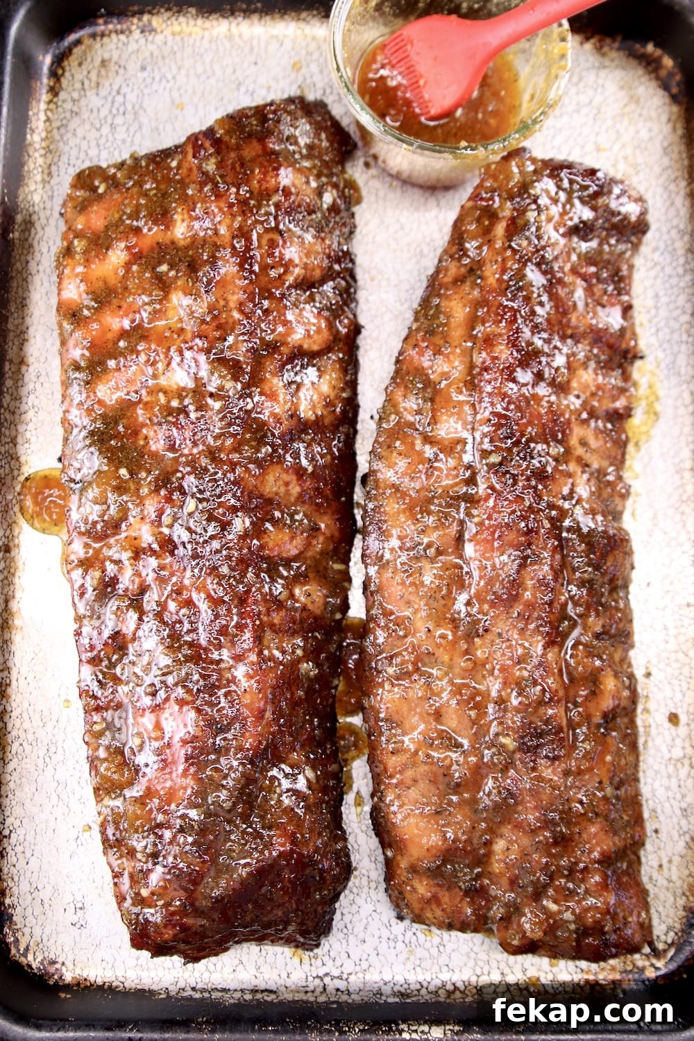 Apricot BBQ ribs with sticky glaze 2 racks of ribs brushed with bbq sauce on a sheet pan with jar of sauce and brush