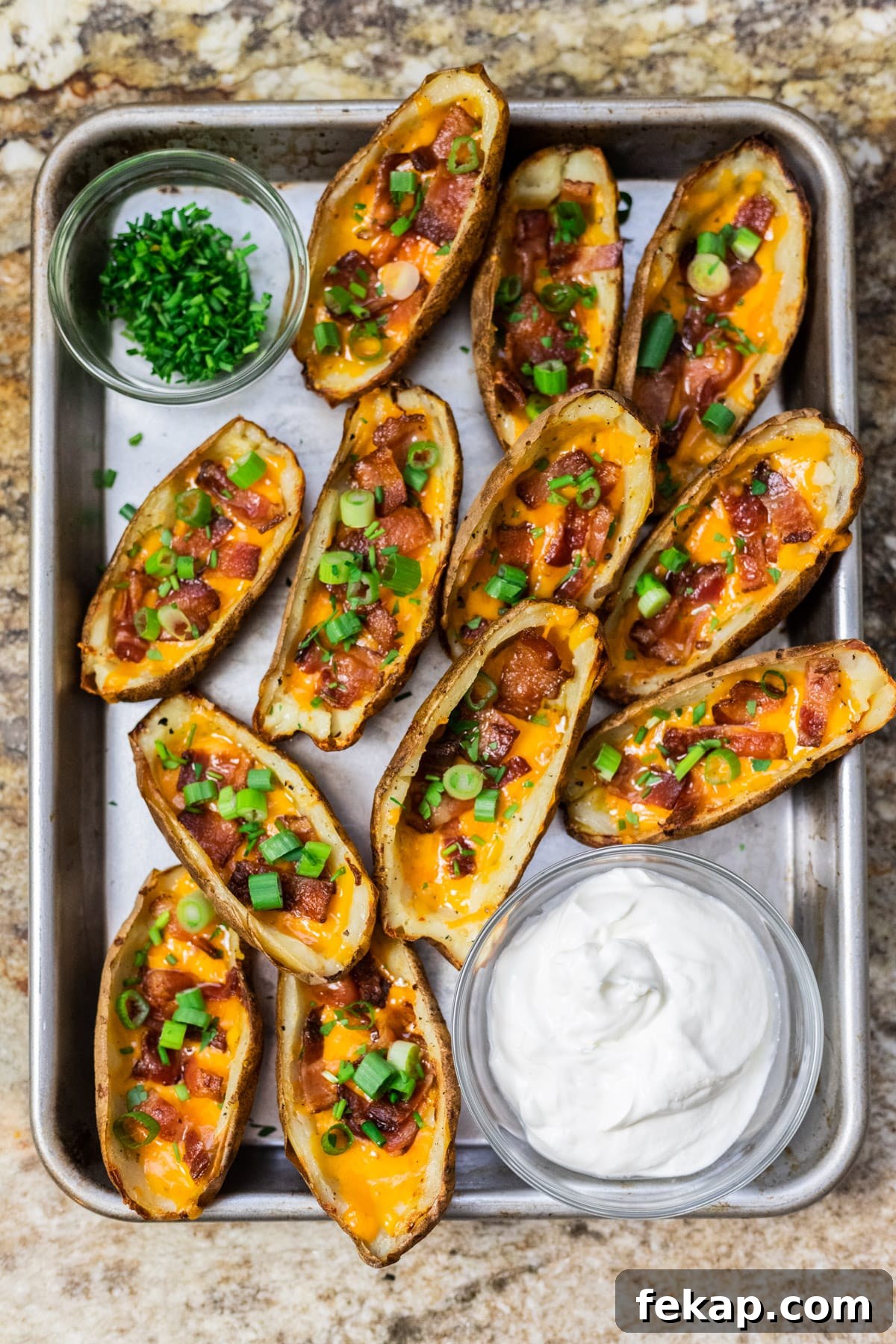 Crispy Potato Skins with Cheddar, Bacon and Green Onions 7 A top down view of loaded potato skins served on a tray with bowls of sour cream and chives.