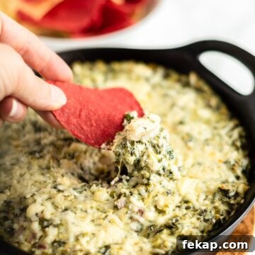 Crispy Potato Skins with Cheddar, Bacon and Green Onions 9 A hand with a tortilla chip scooping up hot spinach and artichoke dip.