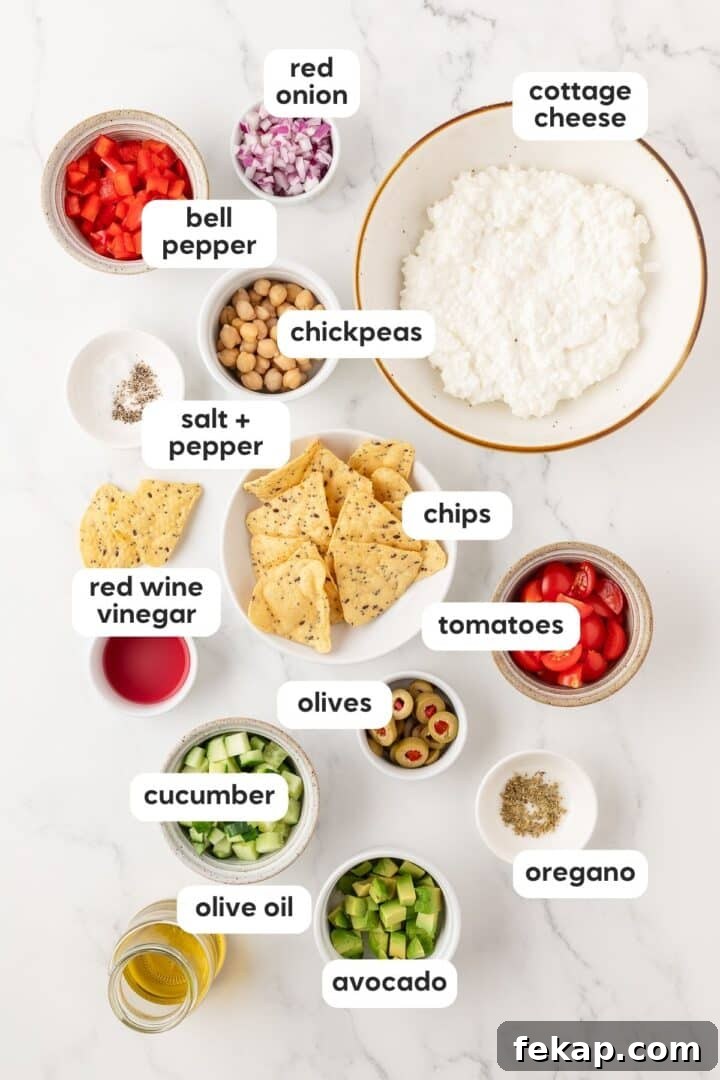 Ingredients for cottage cheese greek salad displayed in small bowls on a white marble counter.