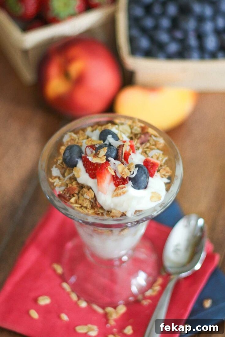 Parfait in tall sundae glass, sitting on red and blue napkins with additional fruit behind.