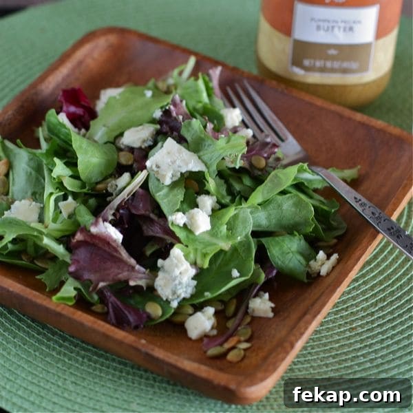 plate of mixed greens topped with pepitas and bleu cheese next to pumpkin butter vinaigrette