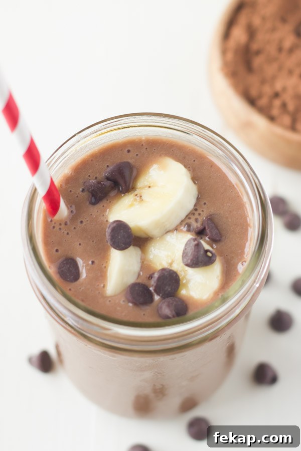 Chocolate Banana Smoothie topped with banana slices and chocolate chips, in a glass jar with a straw.