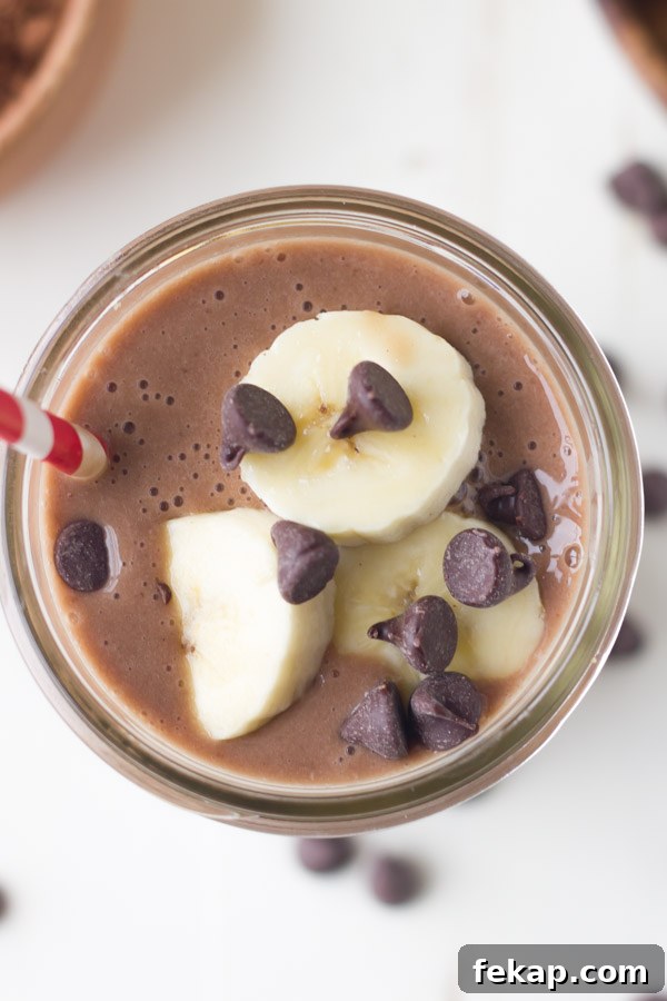 Chocolate Banana Smoothie topped with banana slices and chocolate chips, in a glass jar with a straw.