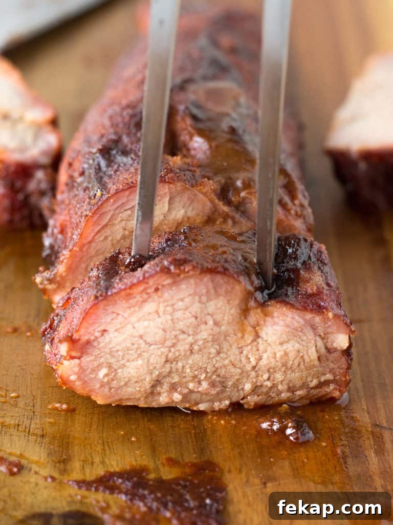 straight on shot of cut up smoked pork tenderloin with a meat fork sticking in the top