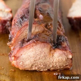 straight on shot of cut up smoked pork tenderloin with a meat fork sticking in the top