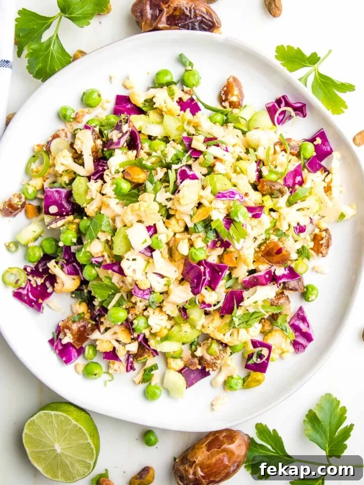 Chopped cauliflower, cabbage, dates and nuts on a round plate with limes and fresh herbs.