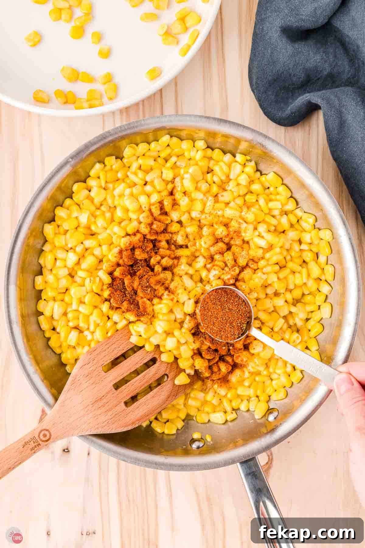 Cajun Fried Corn Recipe: Spicy Southern Side Dish 6 corn in a skillet with a measuring spoon sprinkling seasoning on it