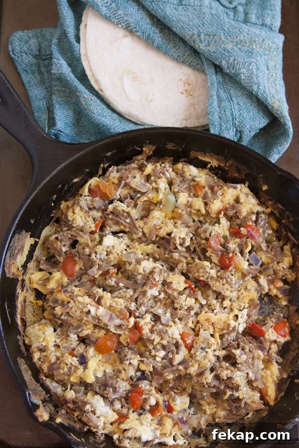 machaca con huevo - Tender shredded beef combined with scrambled eggs, tomatoes, and onions make a delicious skillet breakfast or breakfast burritos. Machaca con huevo recipe cooked in a cast iron skillet with shredded beef, scrambled eggs, tomatoes, and onions, served with warm flour tortillas by Yvette Marquez-Sharpnack of Muy Bueno.