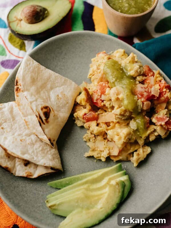 migas on a grey plate with avocado slices and toasted flour tortillas for making breakfast tacos.