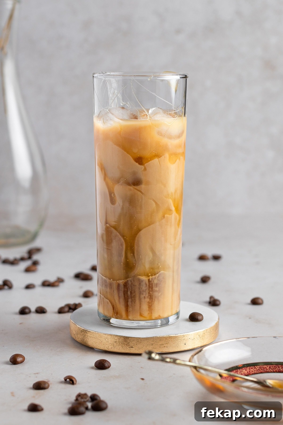 How to Make Caramel Iced Coffee at Home 2 An iced caramel iced coffee in a tall glass, on a white marble table with coffee beans.