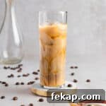 An iced caramel iced coffee in a tall glass, on a white marble table with coffee beans.