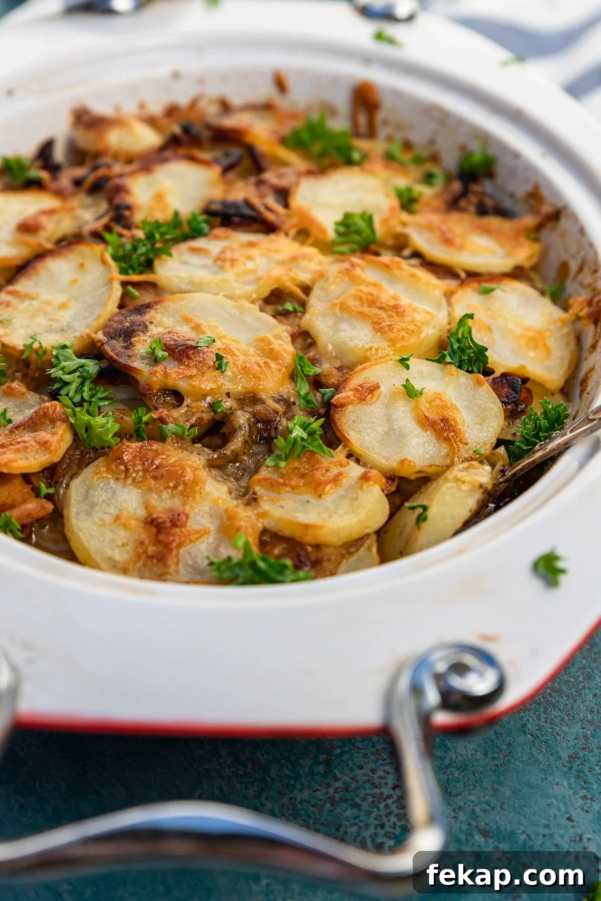 Creamy Bacon Potato Bake Without Cream 2 A closeup of a baking dish of boulangere potatoes or potato bake with bacon with a blue and white stripe tea towel in the background