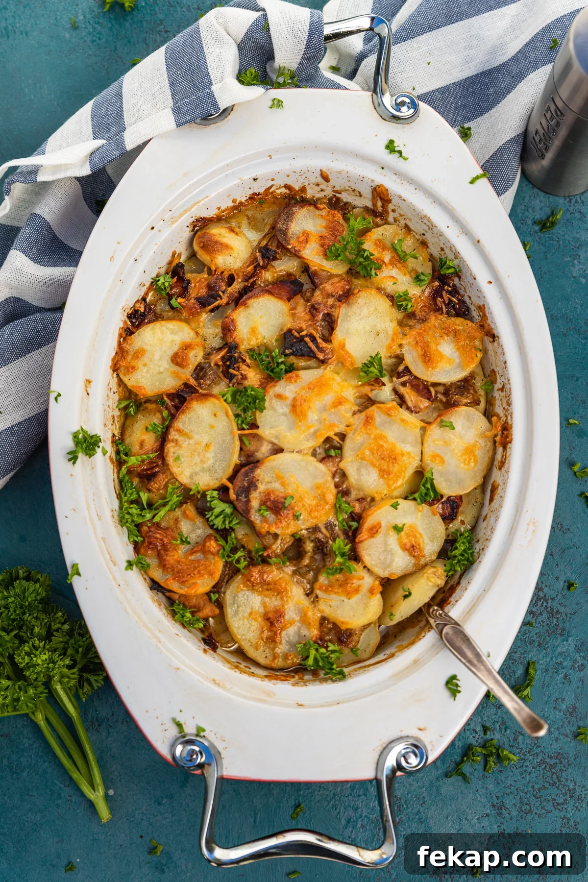 Creamy Bacon Potato Bake Without Cream 6 An oval-shaped baking dish of potato bake with bacon from above on a dark blue background and with a blue and white striped tea towel