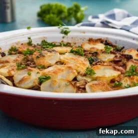 Creamy Bacon Potato Bake Without Cream 8 A red baking dish of boulangere potatoes, or potato bake with bacon, on a blue background and with a blue and white striped tea towel in the background