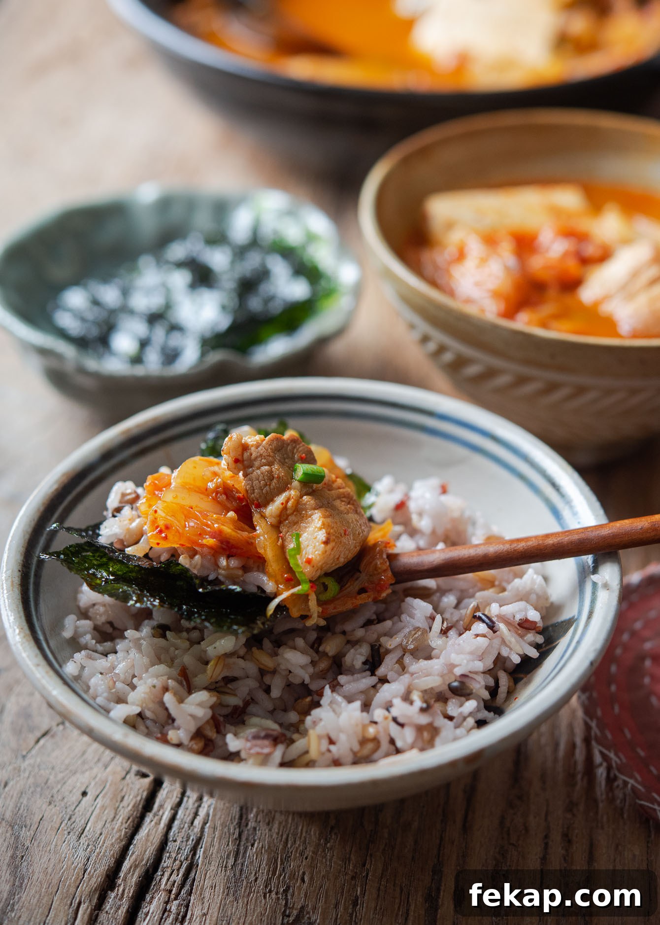Spoonful of rice topped with pork and kimchi jjigae over a bowl of steamed rice.