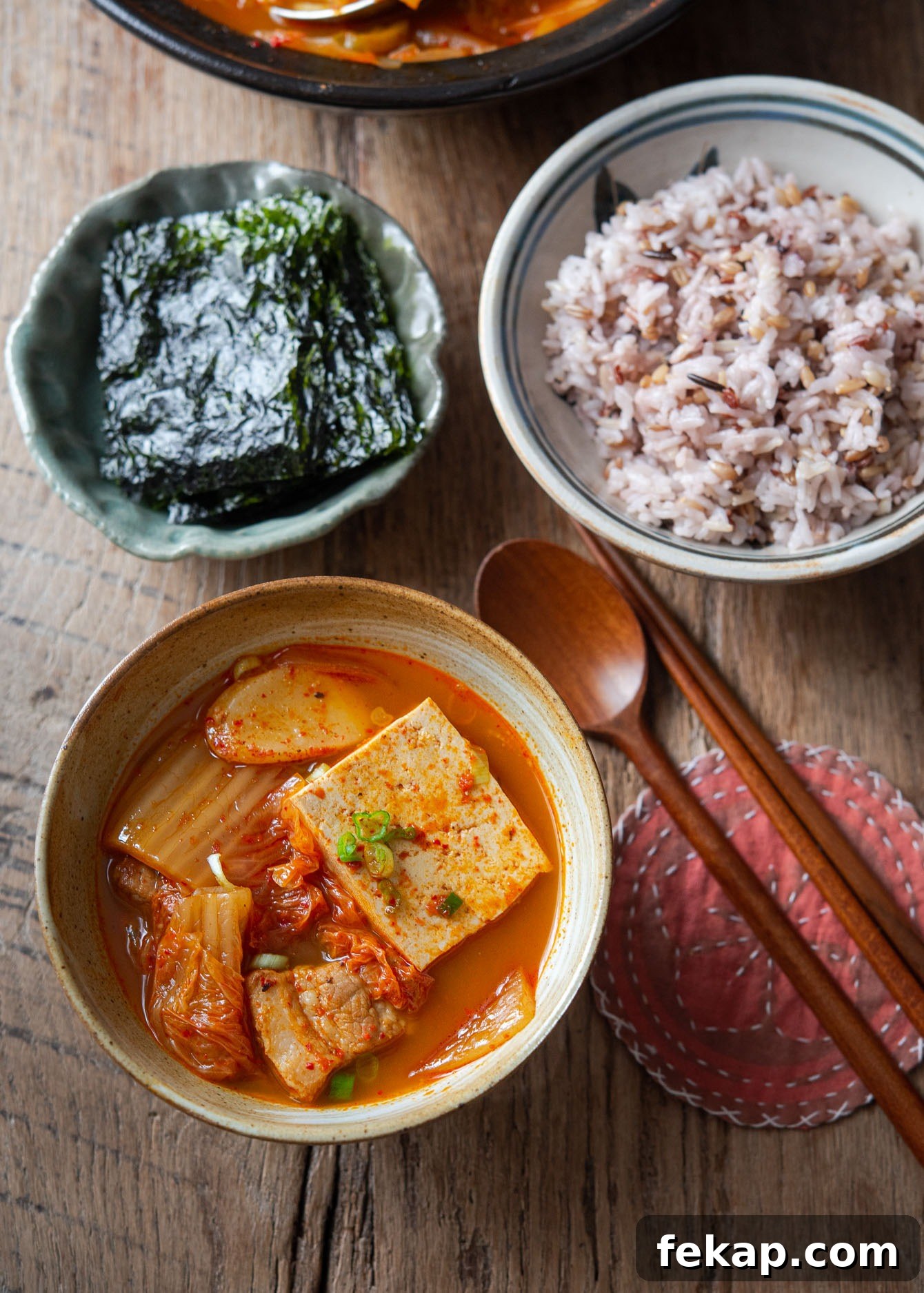 Bowl of kimchi jjigae served with steamed rice and roasted seaweed on the side.
