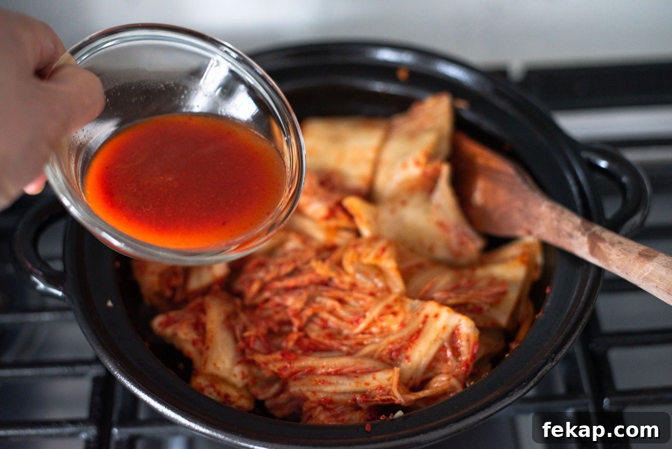 Kimchi juice poured into a pot with sliced kimchi and pork belly for stew.