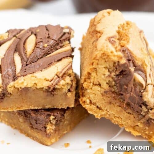 Two thick Brown Butter Blondies with a chocolate swirl on top are stacked on a white plate, with crumbs scattered around them.