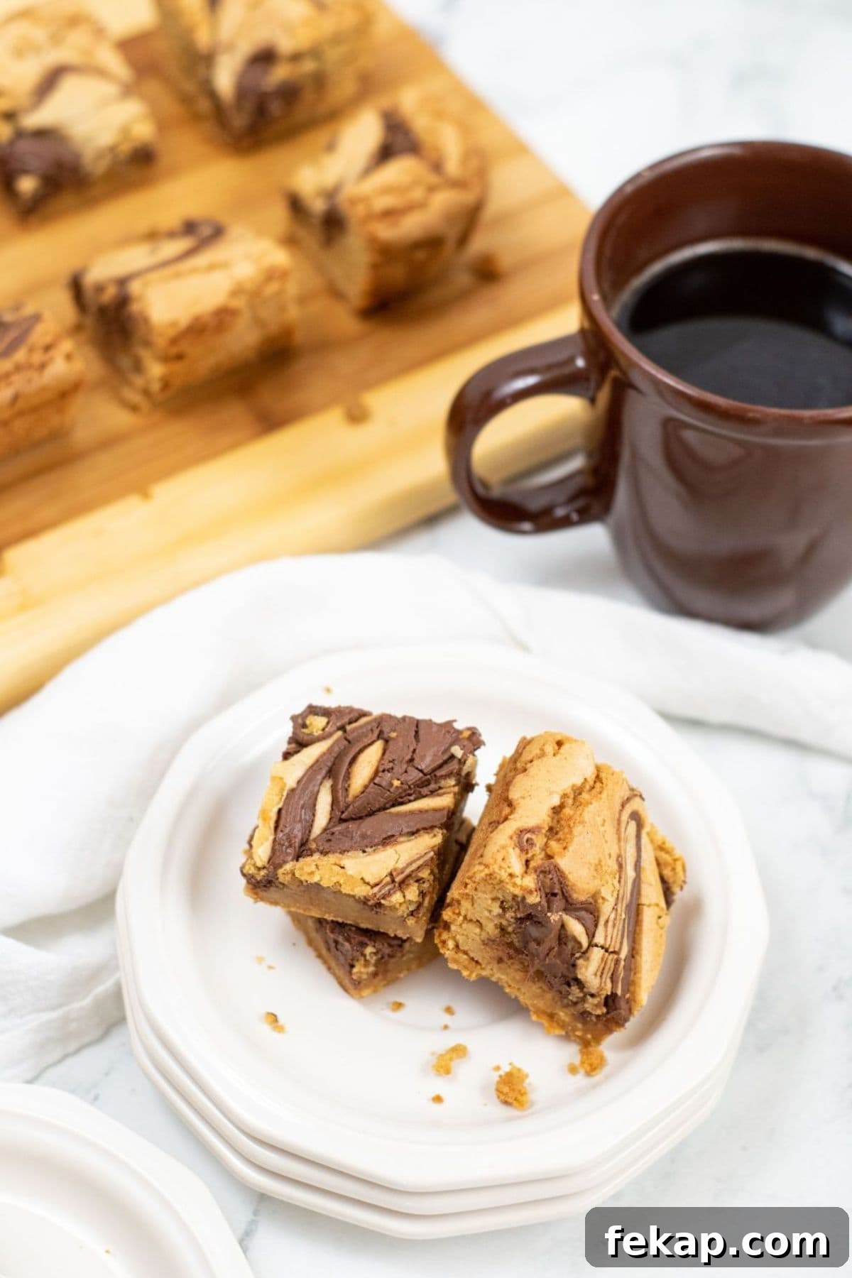 A plate with two squares next to a brown mug of black coffee; more bars are on a wooden board in the background.
