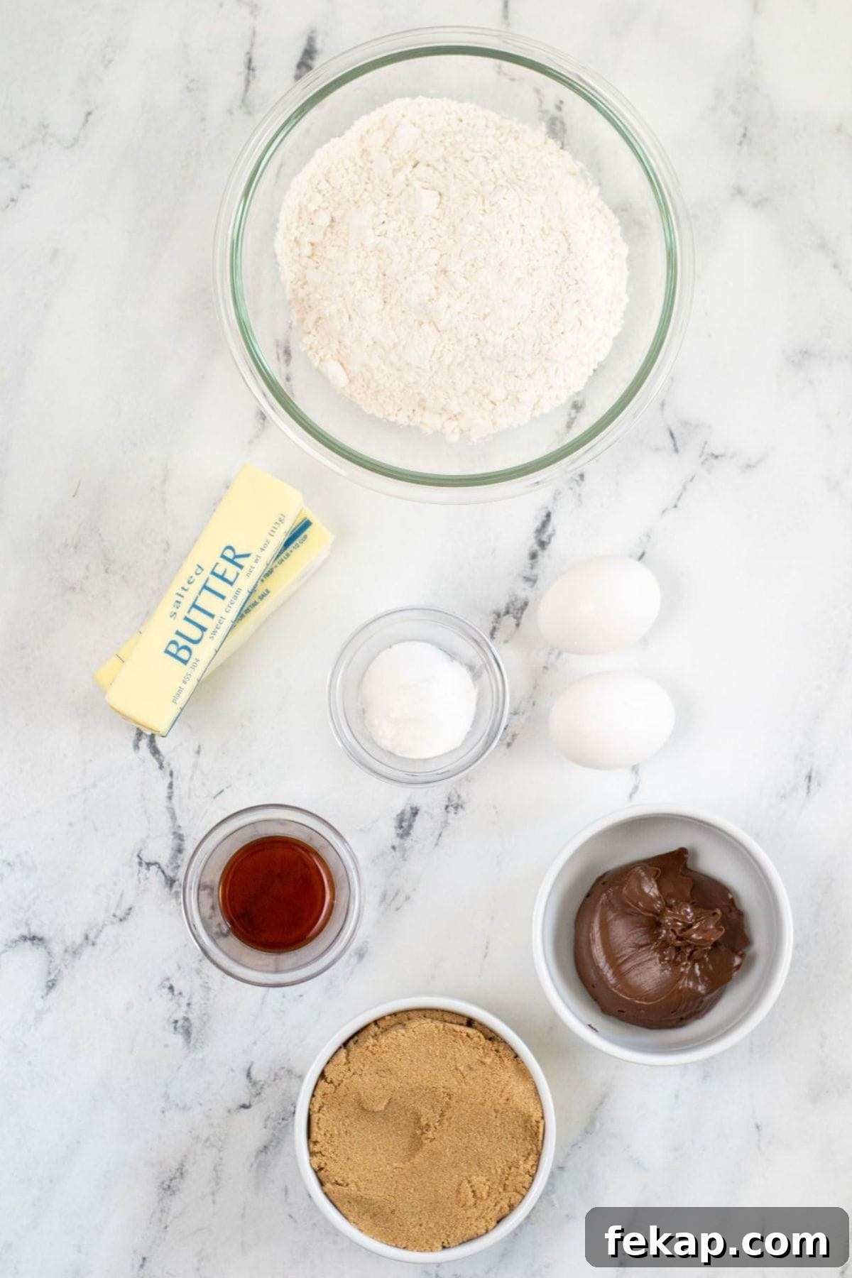 Baking ingredients on a marble surface: flour, butter, baking powder, eggs, vanilla extract, brown sugar, and chocolate spread—all ready to make delicious treats.