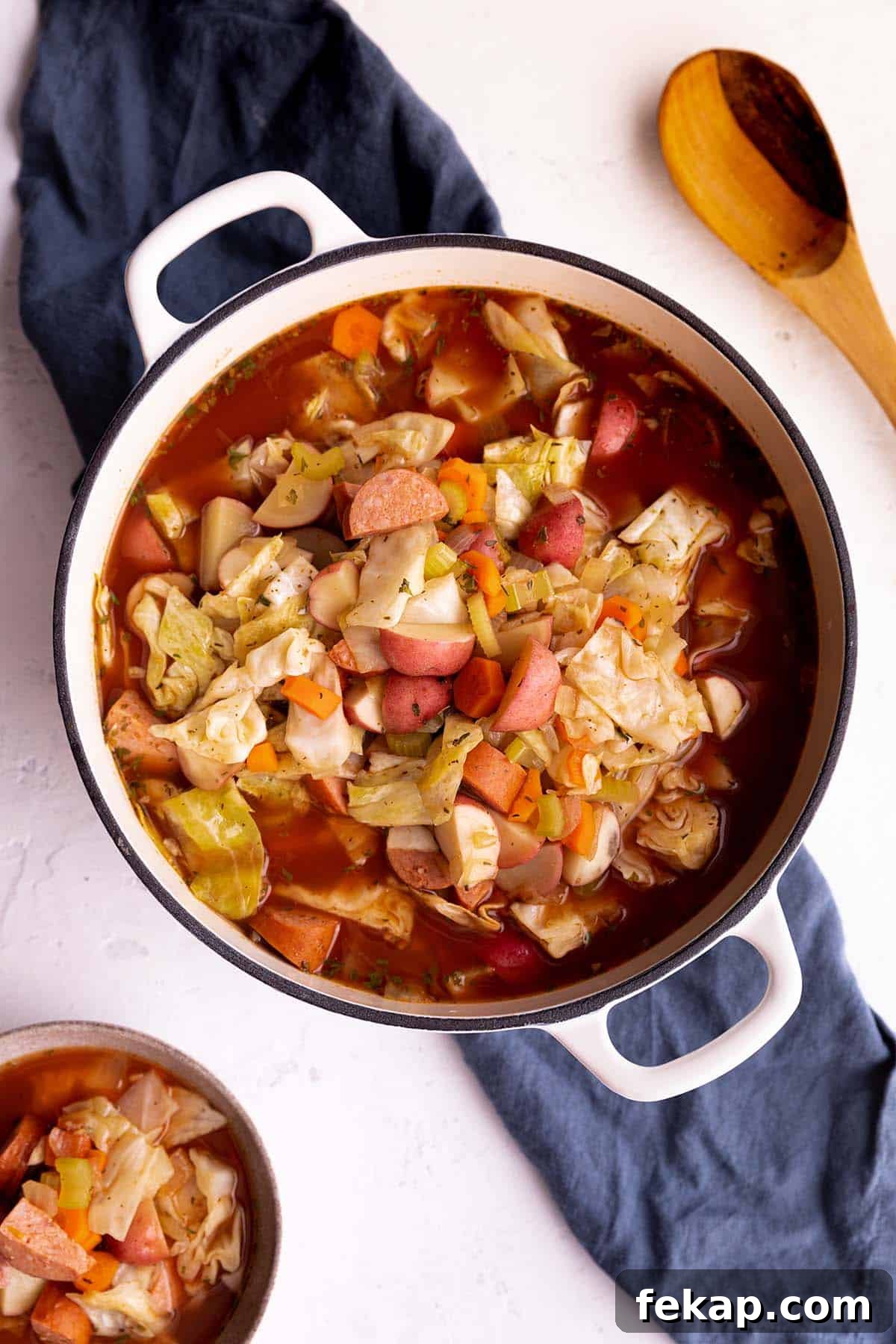 One Pot Cabbage and Sausage Soup Recipe 2 A white dutch oven with a potato, cabbage and sausage soup.