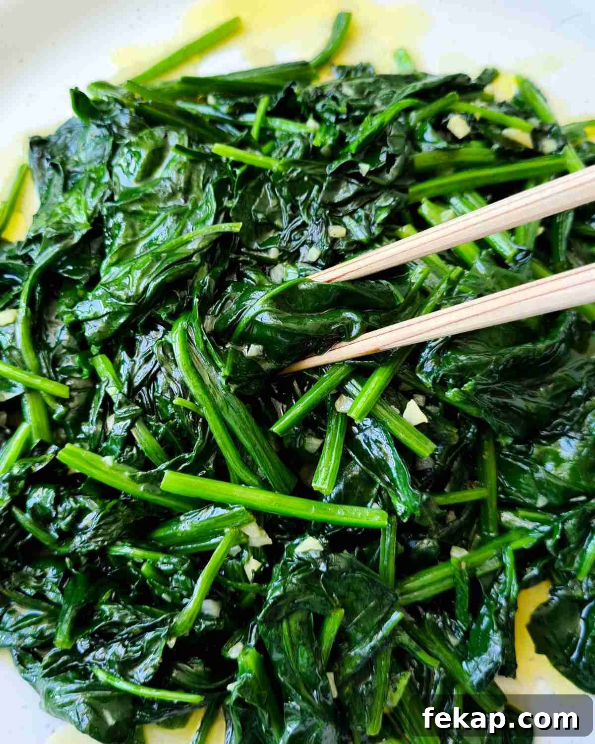 Garlic Stir-Fried Spinach Recipe 10 Close up of stir fried spinach with a pair of chopsticks picking up a piece