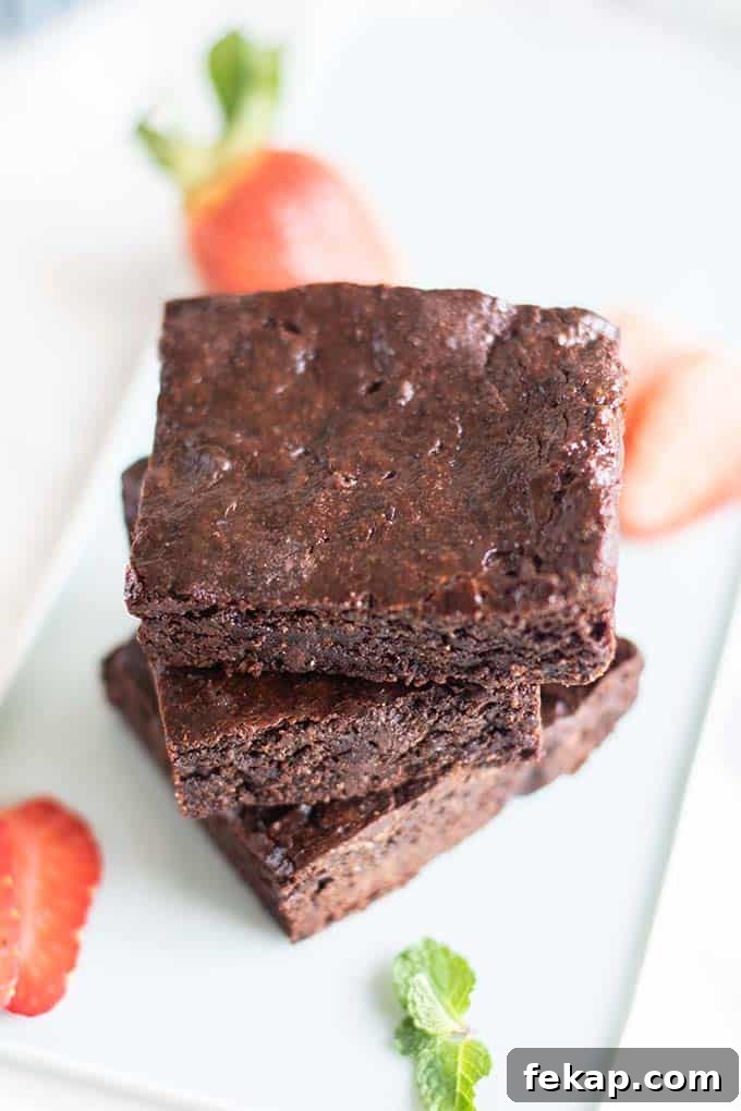 3 fudgy vegan brownies stacked on a blue plate with strawberries.