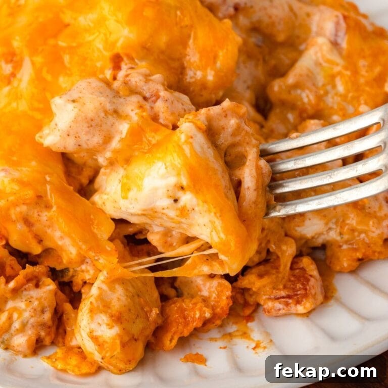 A fork digging into a cheesy Doritos casserole on a white plate.