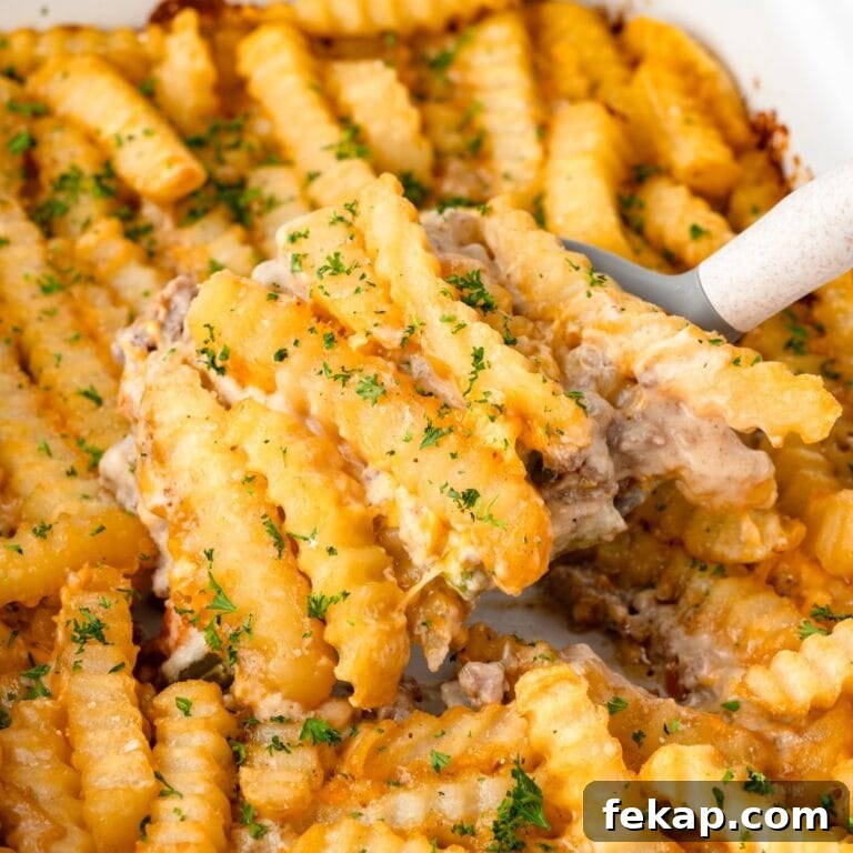 Crinkle-cut fries with melted cheese and ground beef, topped with parsley, served from a casserole dish.