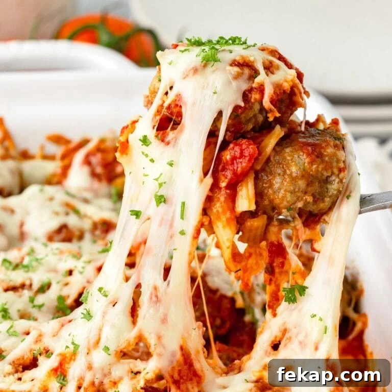 A close-up of a cheese meatball casserole being lifted from a dish, showing melted mozzarella cheese stretching and topped with tomato sauce and chopped parsley.