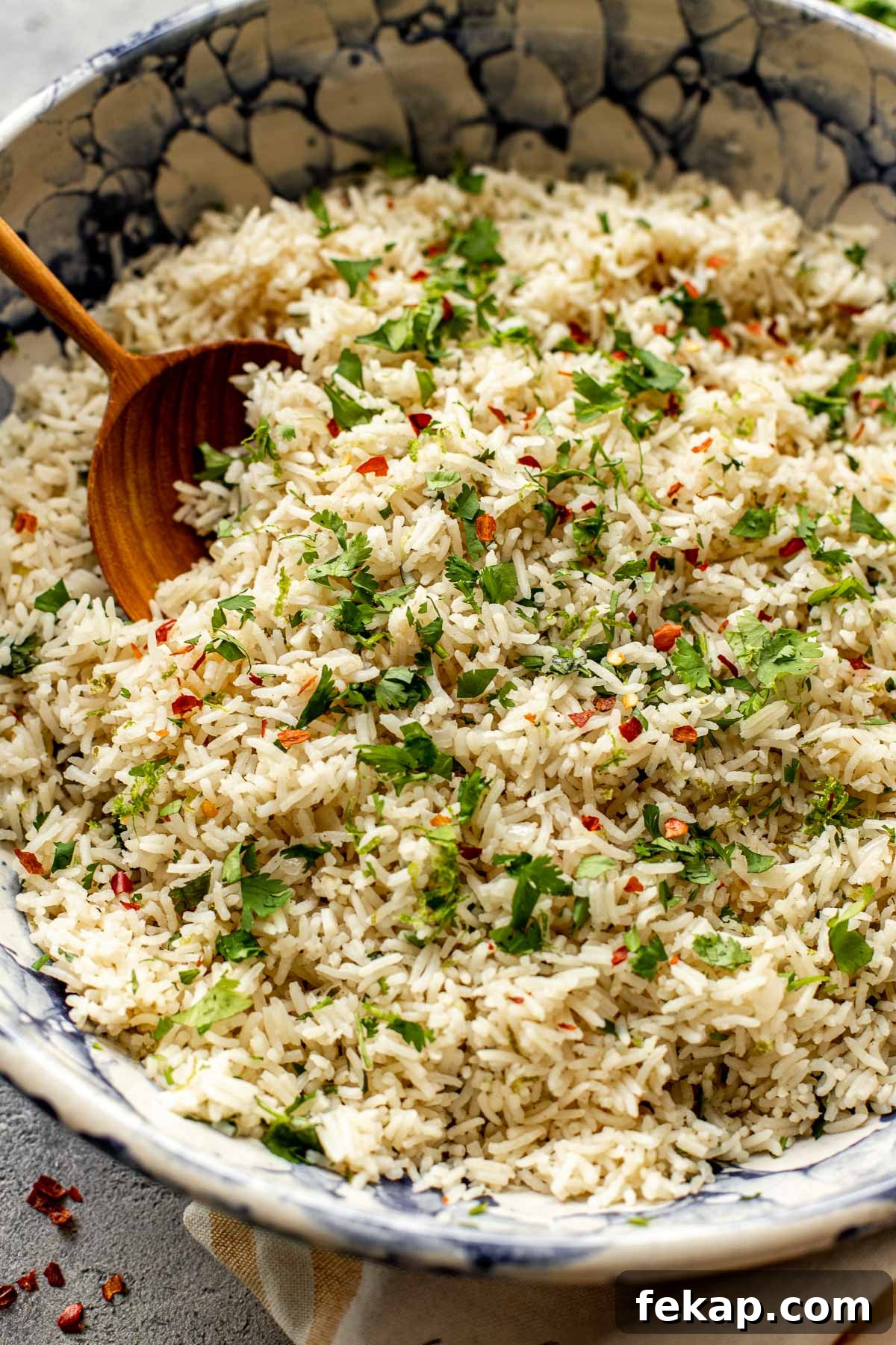 Rice in a blue and white bowl with a wooden spoon garnished with cilantro and red pepper chili flakes. 