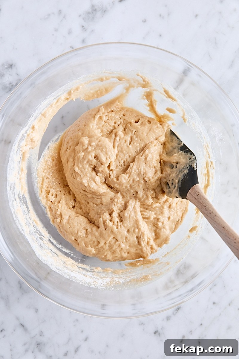 Mixed apple fritter bread batter in large glass bowl with spatula