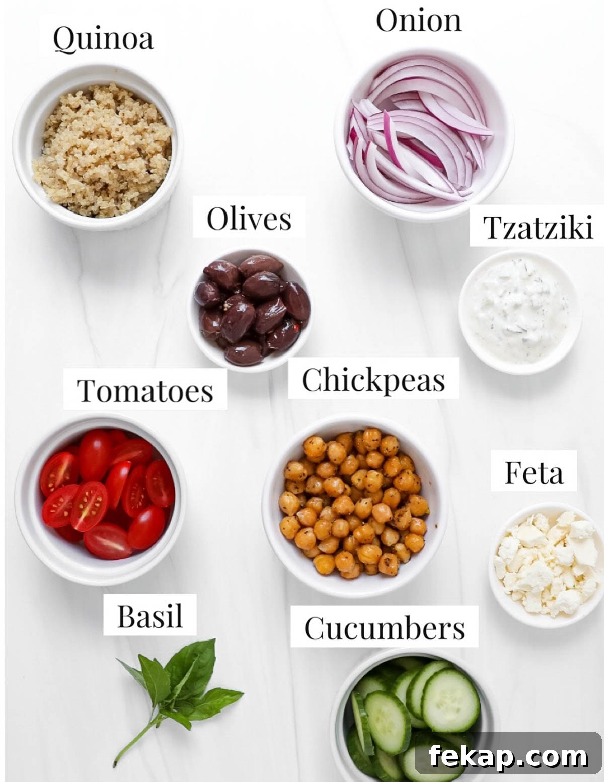 Greek Quinoa Bowl Recipe with Feta, Cucumber and Olives 3 The ingredients for a salad are in small white bowls.