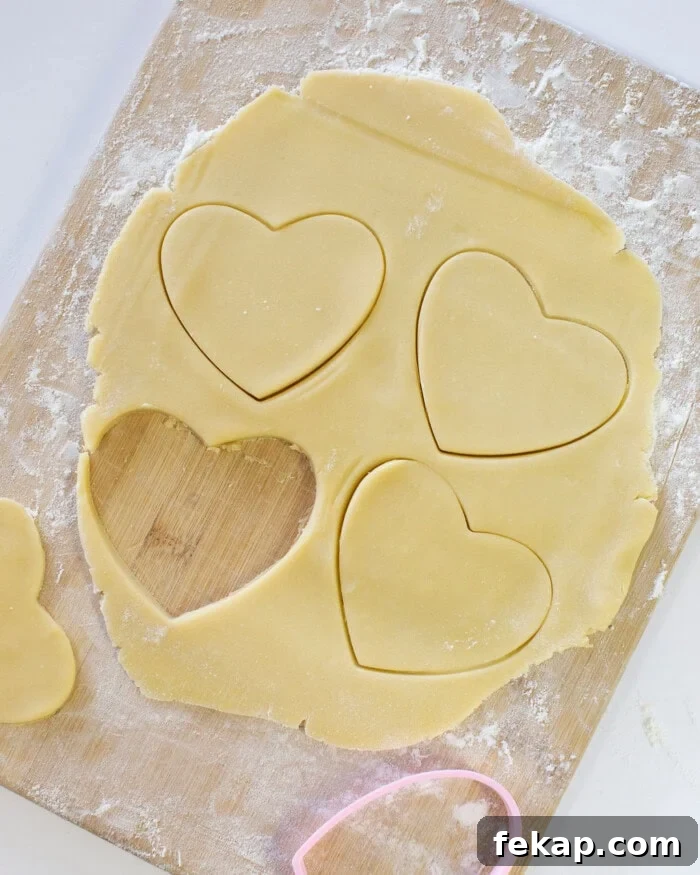 Cut Out Sugar Cookie Recipe for Perfect Shapes 16 Sugar cookie dough rolled out into a thin layer on a wooden cutting board with heart shaped cutouts.